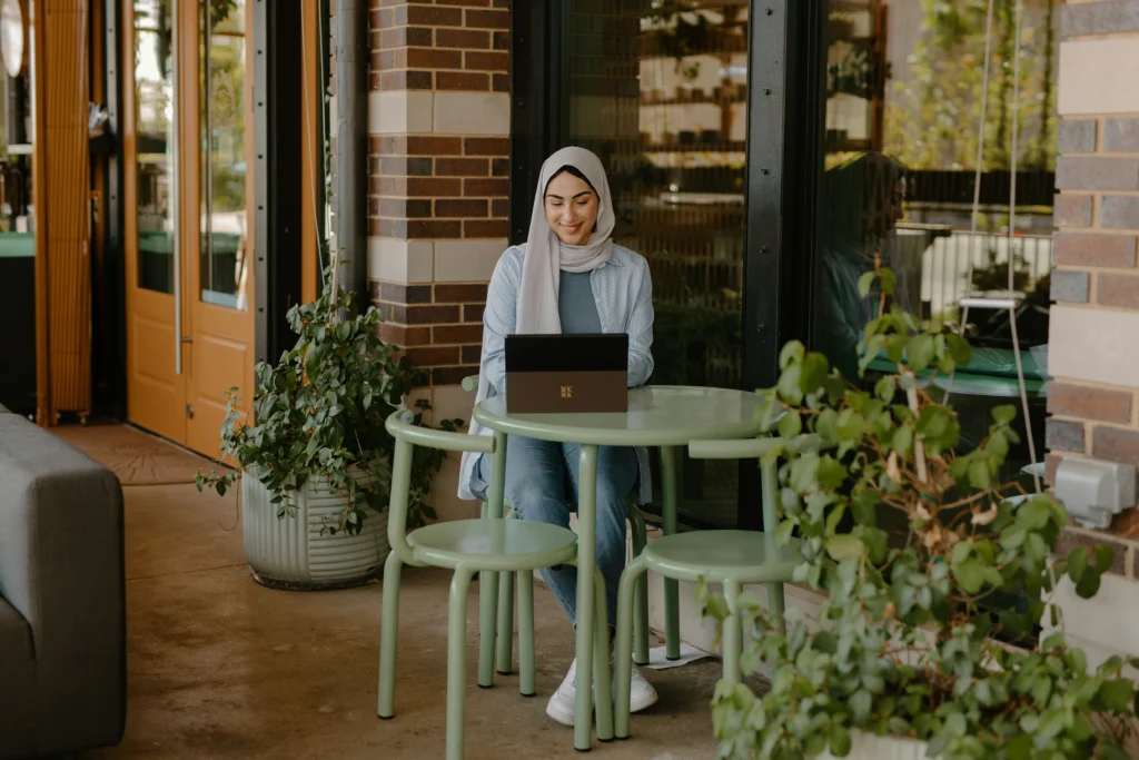 Woman sitting at table in cafe smiling at laptop